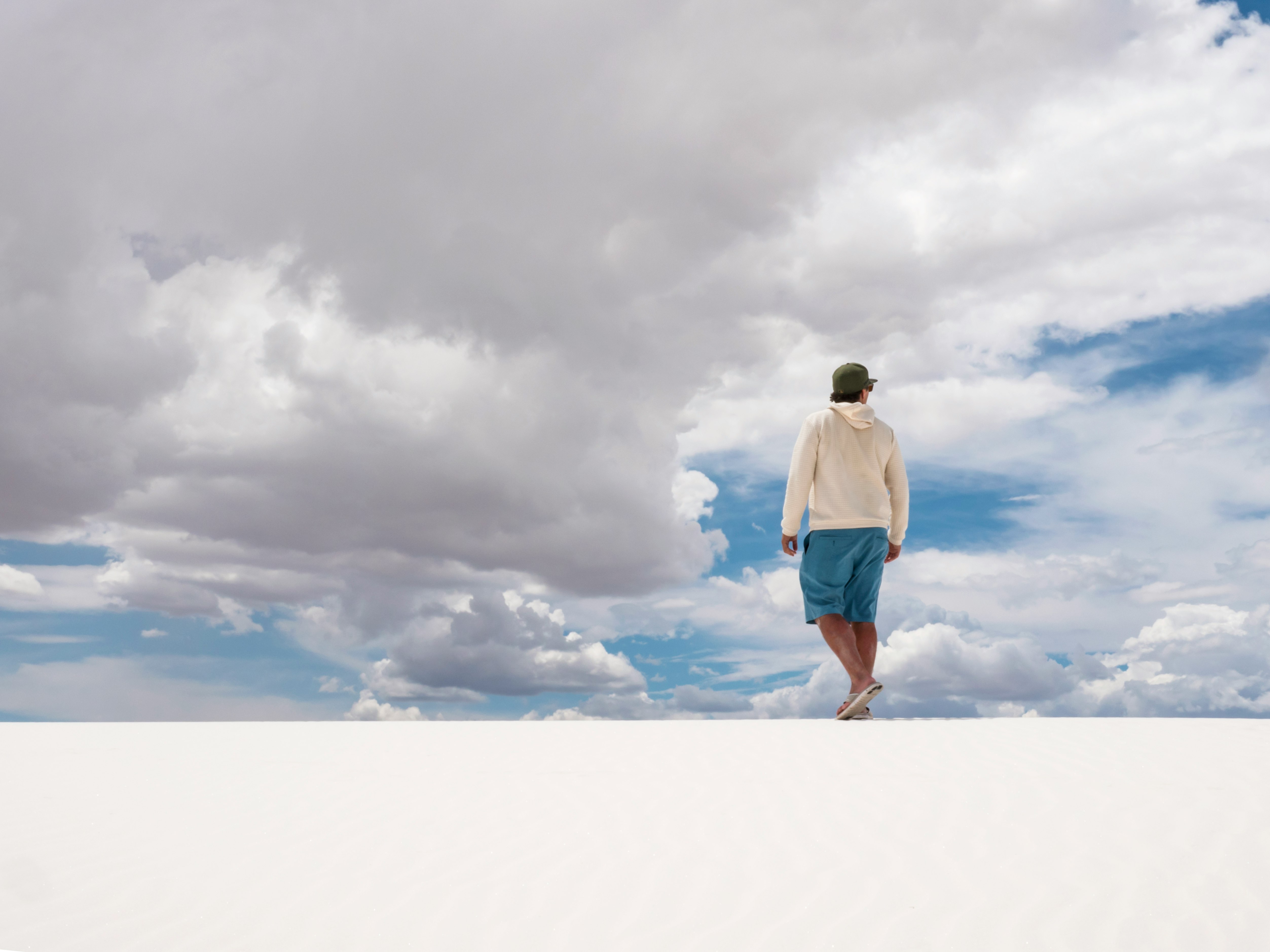 man in white shirt and blue denim jeans standing on white sand under white clouds during